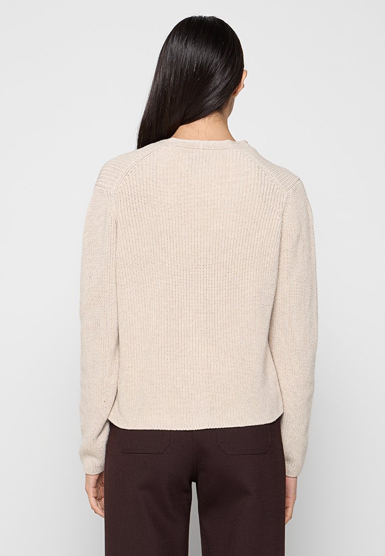 Beige gestrickter Pullover mit strukturiertem Rippmuster, Rundhalsausschnitt und Raglanärmeln, der eine taillierte Silhouette und saubere Kanten aufweist.