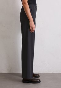 Pantalons noirs taille haute avec une coupe droite, en tissu lisse. Associés à des chaussures sombres et épaisses, mettant en avant un design minimaliste.