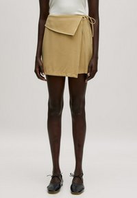 Khaki wikkelrok met een gestrikte taille, voorzien van een klepzak en zachte, gladde stof. Gemaakt met zwarte flats en doorschijnende tights.