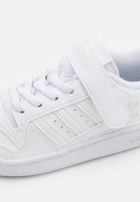 Sneaker bianco con tomaia in pelle testurizzata, dettagli perforati, lacci e una chiusura a strappo. Caratterizzato da una suola in gomma e un branding minimale.