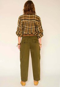 Chemise à carreaux brune avec des manches bouffantes, associée à un pantalon cargo vert olive avec des poches arrière et une coupe décontractée.