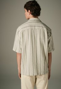 Camisa de manga corta en gris claro y blanco con rayas verticales y patrón texturizado. Cuenta con un collar puntiagudo y un dobladillo recto.