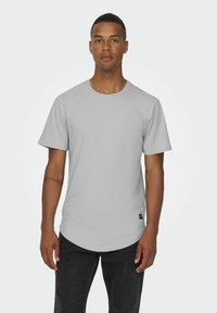 Gray short-sleeve t-shirt with a round neckline, smooth texture, and a curved hem, paired with dark jeans and a small tag at the bottom.