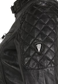 Zwarte leren jas met gequiltte schouderdetails en een klein schildlogo. Gladde textuur met een ritszak aan de zijkant.