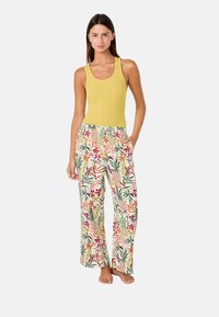Camiseta sin mangas amarilla de canalé combinada con pantalones relajados de corte ancho, coloridos y estampados con diseños florales tropicales y bolsillos laterales.