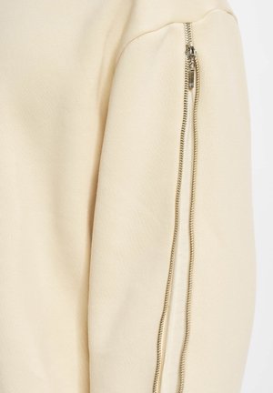 Beige sweatshirt with a textured finish, featuring a zippered accent along the sleeve. Zipper is silver-toned, adding detail to the design.