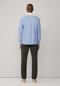 Camisa de botones de color azul claro con cuello blanco, que presenta detalles de rayas verticales en los hombros y las mangas, combinada con pantalones verdes oscuros.