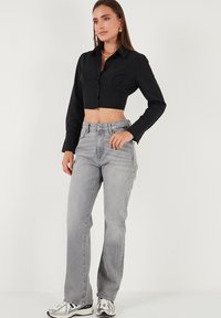 Black cropped button-up shirt with long sleeves, paired with high-waisted light gray jeans and reflective silver sneakers.