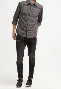 Šedé tričko s dlouhým rukávem s límcem na knoflíky, přední kapsou a růžovými doplňkovými knoflíky, kombinované s černými úzkými džíny a černými teniskami.