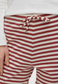 Gros plan sur une personne portant un pantalon à rayures horizontales rouges et blanches avec un cordon de serrage noué, et une chemise blanche à manches longues.