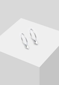 Orecchini a cerchio in argento con un piccolo pendant triangolare appeso a ciascuno. Texture liscia, design minimalista, finitura lucida.
