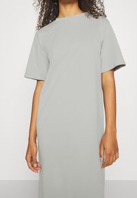 Harmaa, lyhythihainen, pyöreäkauluksinen mekko, joka on valmistettu pehmeästä puuvillakankaasta. Mekossa on rento istuvuus ja sileä pinta. Ei näkyviä kuvioita tai yksityiskohtia.