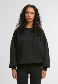 Svart genser med oversized passform, med teksturerte broderte detaljer i form av sommerfuglmotiver på fronten og ermene.