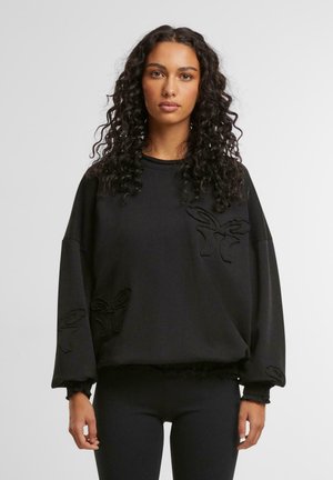 Svart sweatshirt med översize-passform, med texturerade broderade detaljer i form av fjärilsmotiv på framsidan och ärmarna.