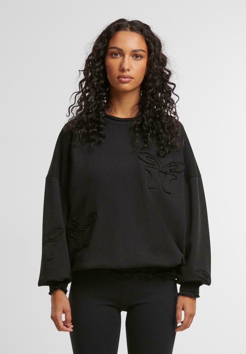Svart genser med oversized passform, med teksturerte broderte detaljer i form av sommerfuglmotiver på fronten og ermene.