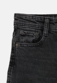 Svarta denimjeans med en klassisk femfickdesign, koppardetaljer och en texturerad yta på tyget.