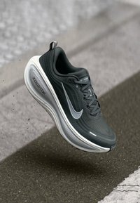 Μαύρο αθλητικό παπούτσι με υφή στο πάνω μέρος, διαθέτει ασημένιο λογότυπο Nike και λευκή ενδιάμεση σόλα, σχεδιασμένο για άνεση και υποστήριξη.