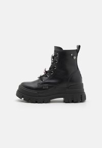 Botas negras hasta el tobillo con suela gruesa, material de cuero, diseño con cordones y charms decorativos en el costado. Parte superior texturizada y construcción robusta.