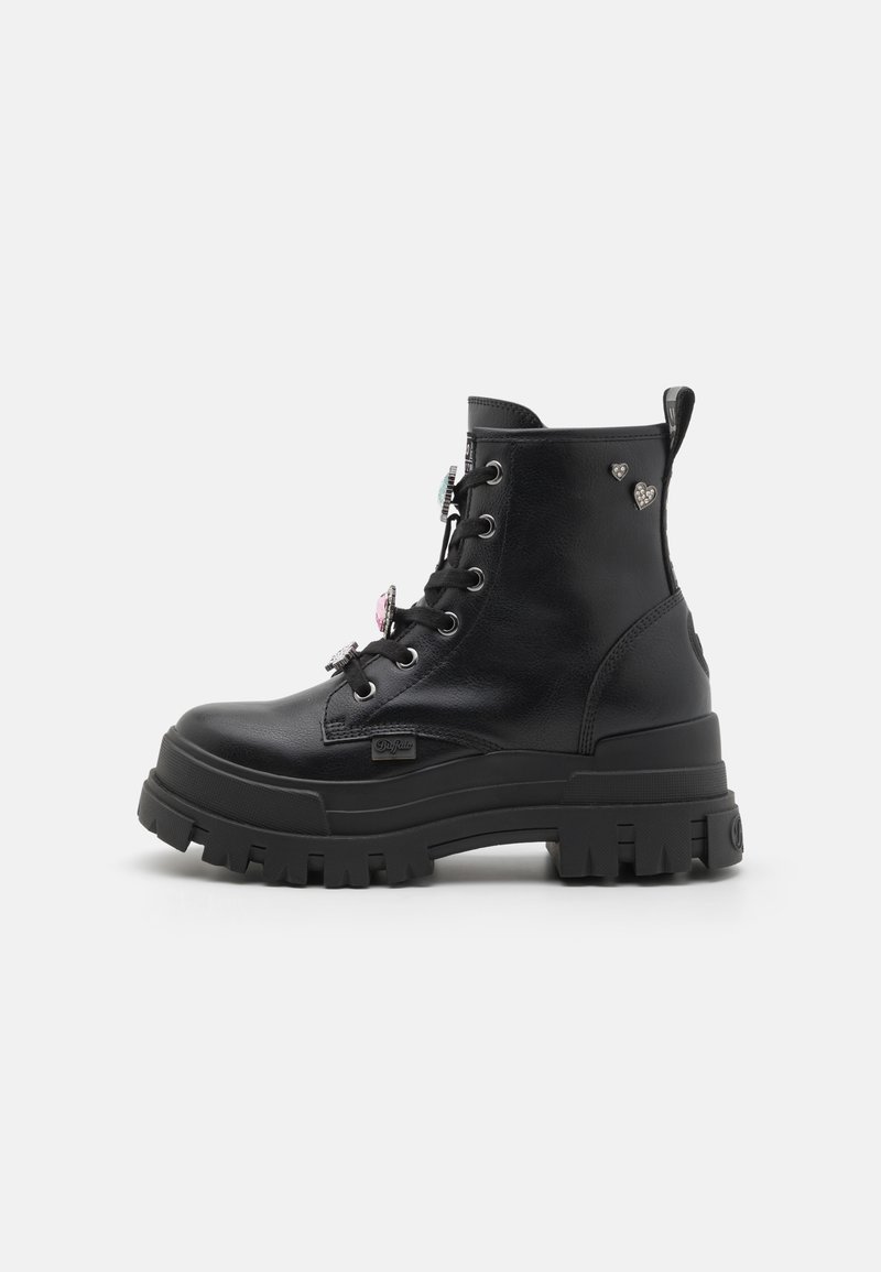 Botas negras hasta el tobillo con suela gruesa, material de cuero, diseño con cordones y charms decorativos en el costado. Parte superior texturizada y construcción robusta.
