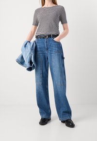 Jeans de mezclilla azul de pierna ancha con bolsillos frontales, combinados con una camiseta de manga corta a rayas blancas y negras, y una chaqueta de mezclilla azul claro.