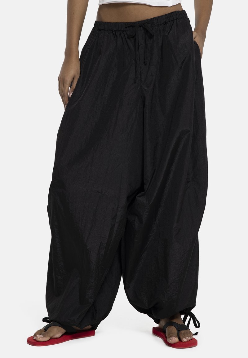 Pantalones sueltos negros con cordón y piernas estilo globo, combinados con sandalias negras y rojas de punta abierta, llevados con un top blanco corto.