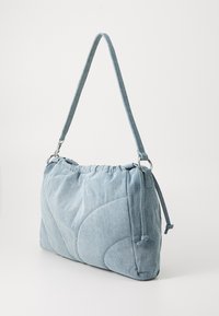 Světle modrá, prošívaná látková taška přes rameno s staženým vrchem, odolným popruhem a detaily ze stříbrného kovu. Kompakt a zaoblený design.