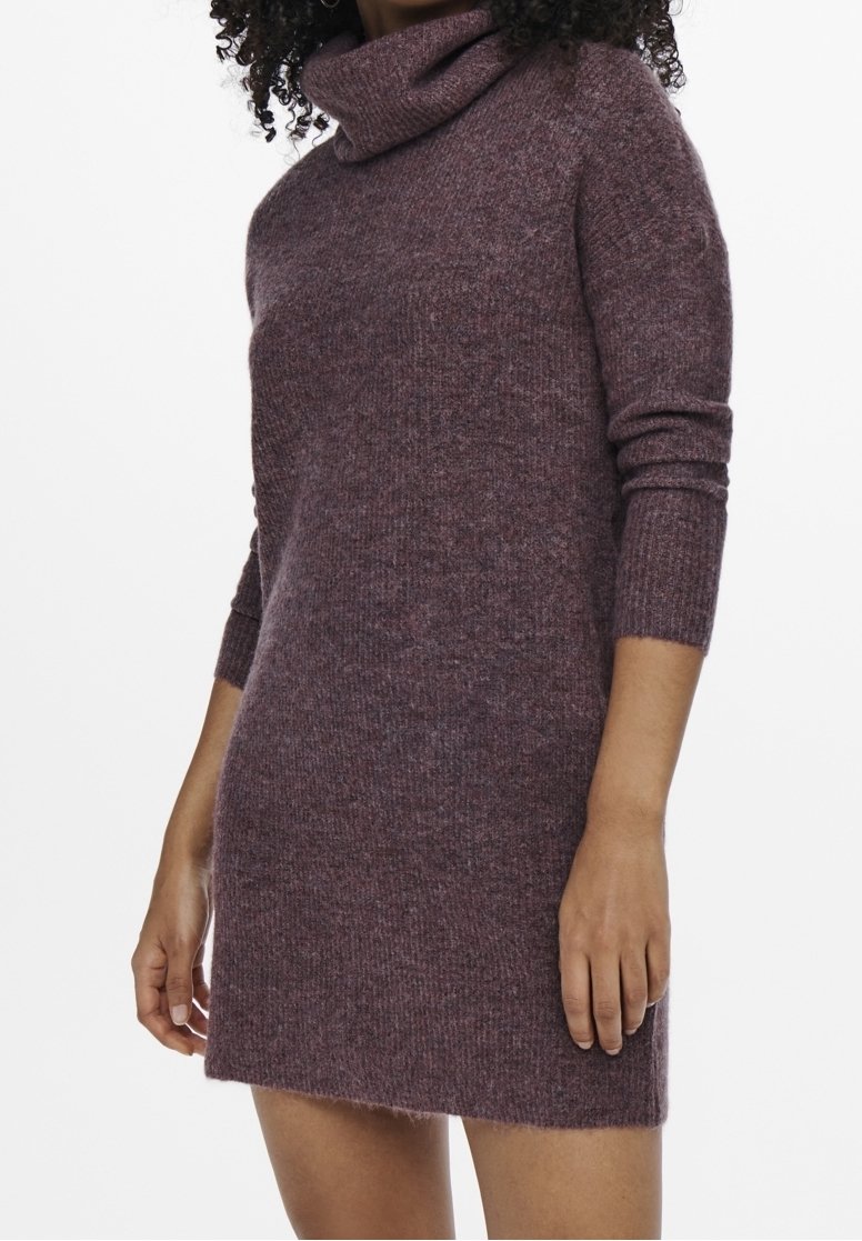 Femme portant une robe en maille à col roulé violet à manches longues, avec une texture douce et pelucheuse, vue des épaules jusqu'à mi-cuisse.