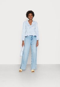 Top peplum com estampa floral azul claro e decote em V, combinado com jeans largos azul claro com fendas laterais e sapatos abertos amarelos.