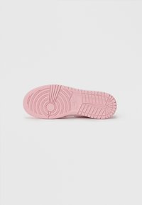 Nike sneaker talpája puha rózsaszín gumiból készült, texturált tapadási mintával, amely kör- és vonalformákat tartalmaz, valamint egy kör alakú logót.