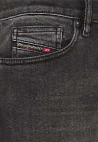 Svarta denimjeans med en bakficka som har en röd och vit "Diesel Industry"-etikett, strukturerad tyg och synliga sömmar.