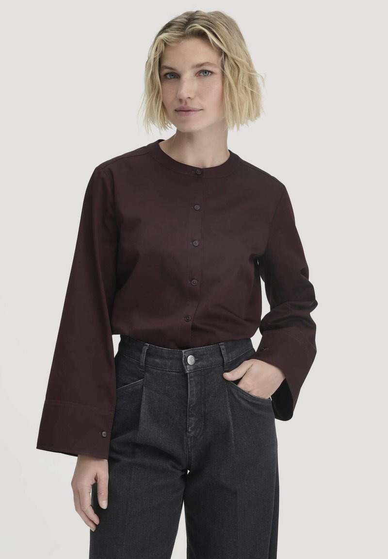 Camicia bordeaux con colletto rotondo e maniche lunghe a campana, abbinata a pantaloni neri a vita alta con tasche laterali.