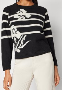 Maglione a righe bianche e nere con motivo floreale, realizzato in tessuto morbido, con collo rotondo e polsini a costine sulle maniche e sull'orlo.