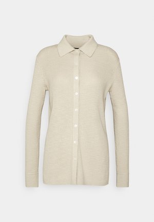 Beige pitkähihaiset ribbineulosnapillinen neuletakki kauluksella, esitetty yksivärisellä vaaleanharmaalla taustalla.