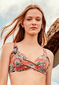 Haut de bikini corail avec un design à motifs en noir et blanc. Doté d'un décolleté en V, de larges bretelles et d'un devant croisé. Texture lisse.