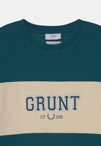 Swtetr w kolorze morskim i kremowym z prążkowanym dekoltem oraz grafiką z napisem "GRUNT" i "EST 2008" w wyraźnym stylu.