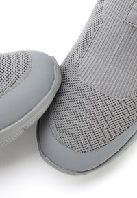 Nahaufnahme von zwei grauen Slipper-Sneakern mit Strickstoff und Gummisohlen auf einem weißen Hintergrund.