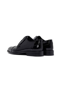 Chaussures noires en cuir verni avec un bout arrondi, un design élancé, un laçage minimal et une semelle en caoutchouc noire légèrement surélevée.