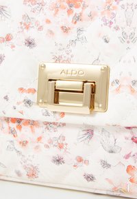Blommig handväska med guldfärgad metalldetalj, med ett quiltat mönster i pastellfärger, främst vit med rosa och orange inslag.