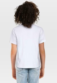 Hvit kortermet t-skjorte med rund hals, antrukket med lyseblå denimjeans, viser en enkel bakvy og myk bomullstekstur.