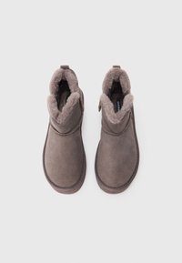 Botas de ante marrón sin cordones con forro de piel suave y punteras redondas, presentadas una al lado de la otra sobre un fondo blanco plano.