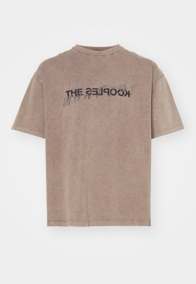T-shirt en coton marron avec un col rond. Le devant présente un texte courbé noir et des accents argentés. Manches courtes avec une coupe décontractée.