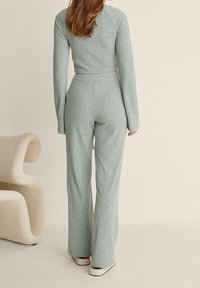 Conjunto de dos piezas de color verde claro con textura acanalada, compuesto por una blusa de manga larga y pantalones acampanados. Material suave y diseño ajustado. Estilo minimalista sin marcas visibles.