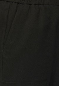 Pantalons en tissu noir avec une finition texturée, dotés d'une taille élastique et de poches latérales. Design simple, couleur unie.