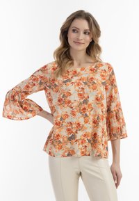 Blomstret bluse i orange og beige med klokke�ærmer, lavet af et let, tekstureret materiale og med en afslappet pasform. Blomsterdesign dækker stoffet.