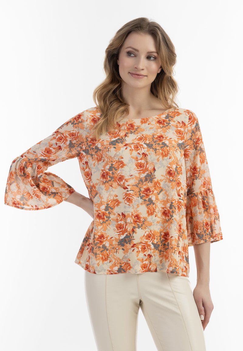 Blomstret bluse i orange og beige med klokkeærmer, lavet af et let, tekstureret materiale og med en afslappet pasform. Blomsterdesign dækker stoffet.