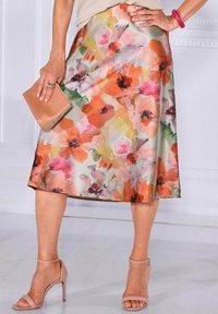 Blumen-Midi-Rock mit fließendem Design in Pastellfarben, das Pfirsich-, Rosa- und Grüntöne umfasst. Kombiniert mit nudefarbenen High-Heels.