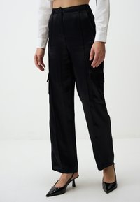 Zwarte satijnen cargobroek met een losse pasvorm, voorzien van zijzakken en een gladde textuur. Gecombineerd met zwarte puntige slingback hakken.