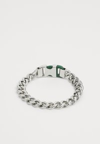 Bracciale in metallo argentato con design a catena intrecciata, dotato di un accent in gomma verde sulla chiusura. Texture liscia e finitura lucida.