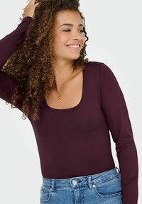 Body a manica lunga bordeaux con scollatura a barca, realizzato in tessuto morbido, abbinato a jeans in denim blu con vestibilità classica e dettagli delle tasche.