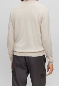 Helle beige Strickpullover mit Rundhalsausschnitt und langen Ärmeln. Hat eine taillierte Taille und Bündchen. Glatte Textur mit minimalen Details.